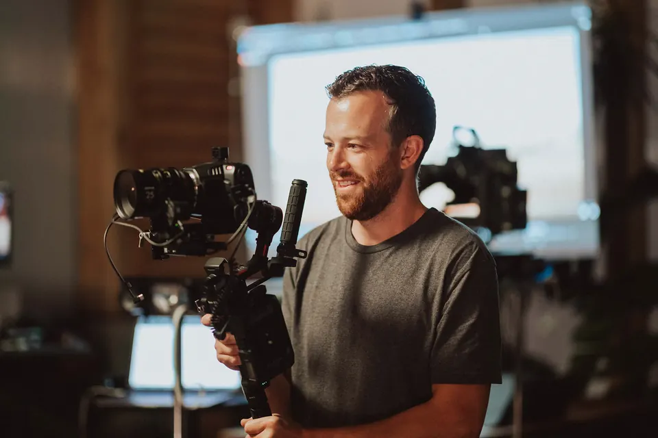 Jared Henderson running camera on set with a monitor and lights