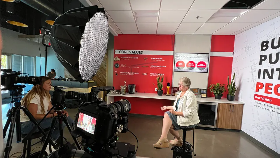 Interview set with camera and lights in front of a red "Build Purpose Into People" wall