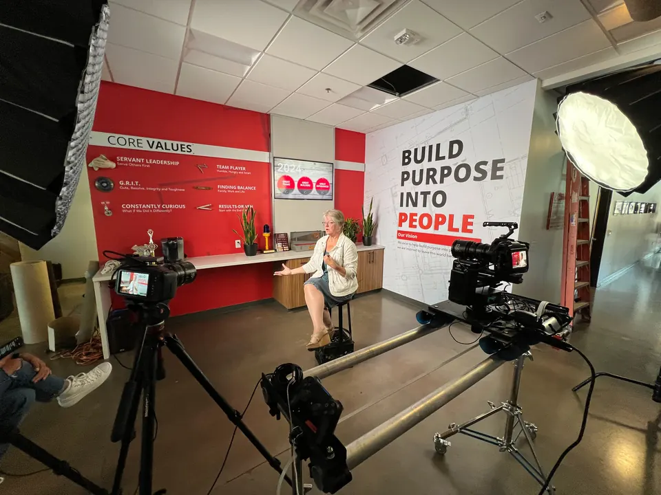 Interview set with lights and cameras in front of a red "Build Purpose Into People" wall