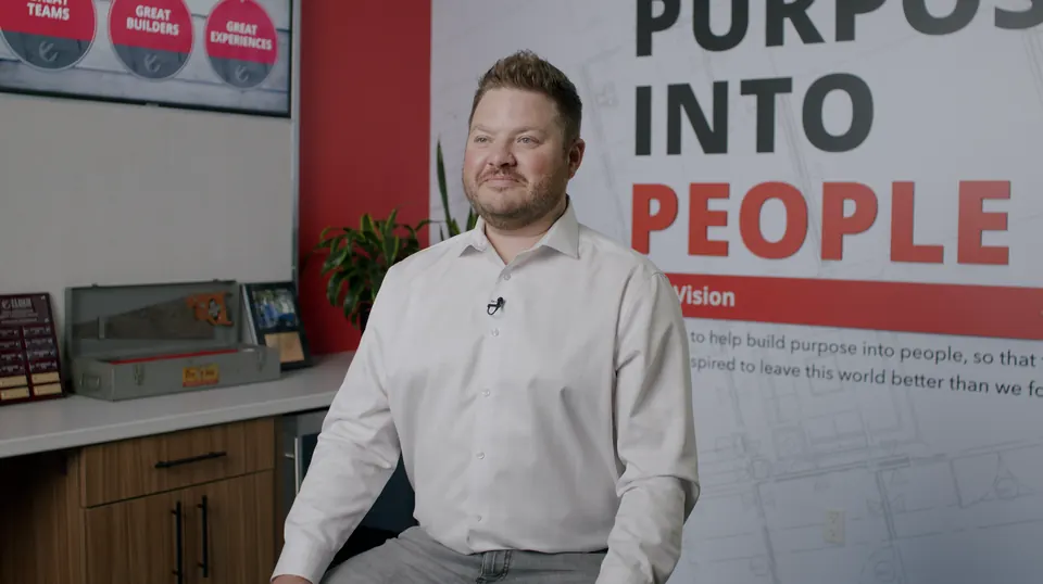 Man interviewed on camera in front of the "Purpose Into People" wall