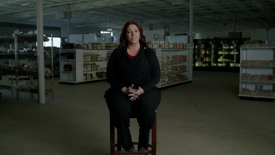 Interview subject seated in a wide warehouse shot with shelving behind