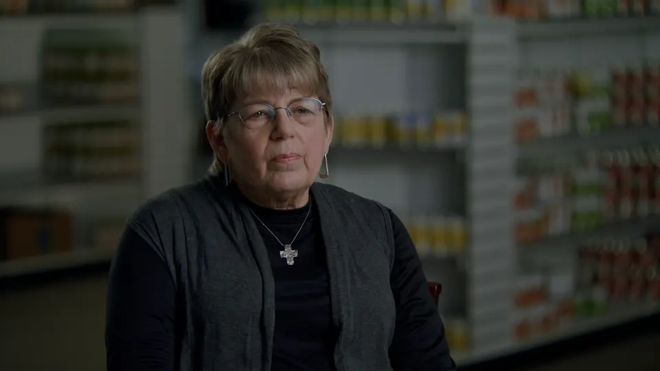 Older woman interviewed in front of stocked shelves