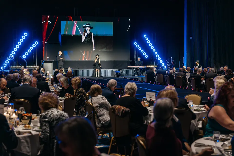 Guests at round tables in the ballroom under blue stage lighting