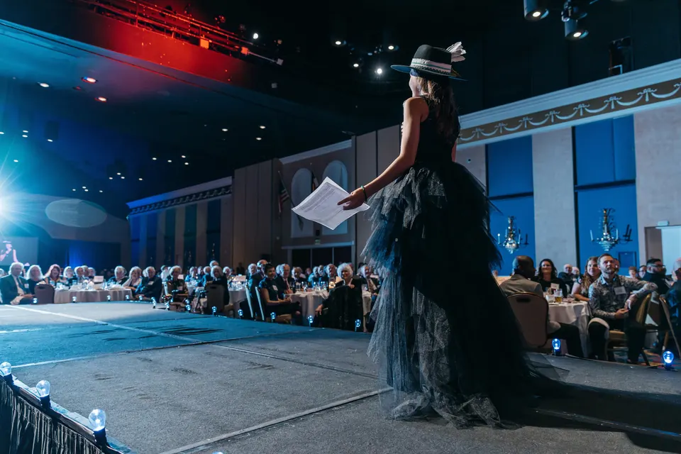 Model in a black gown on the runway as guests watch