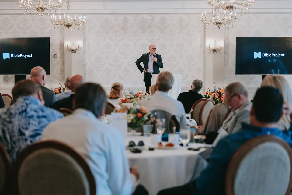 Speaker standing among the tables with slides on two screens